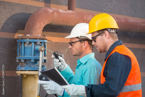young men and a woman are standing near the gas pipe at the house with an analyzer and documents, checking the gas leak. Are they inspectors or engineers.