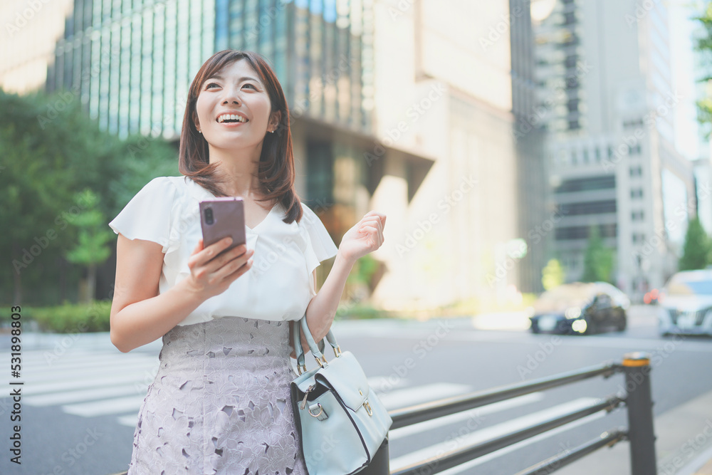 オフィス街でスマートフォンを操作しながら待ち合わせをする女性 オフィス街でスマートフォンを操作しながら待ち合わせをする女性