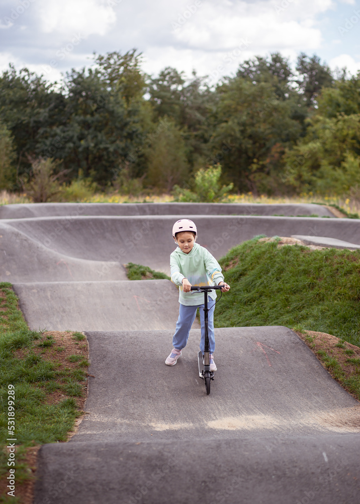 portrait of cute little caucasian school girl wear helmet enjoy having fun riding scooter on asphalted track.in street park outdoors on sunny day. Healthy sport children activities outsid portrait of cute little caucasian school girl wear helmet enjoy having fun riding scooter on asphalted track.in street park outdoors on sunny day. Healthy sport children activities outsid