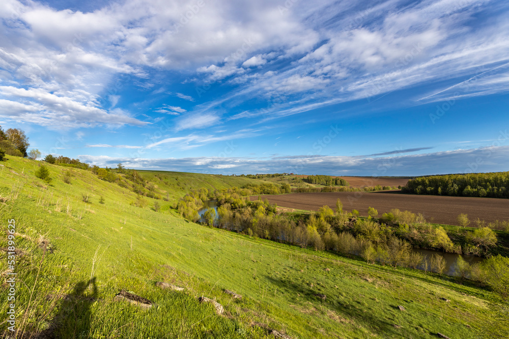 Naklejka premium View of the countryside. bright greenery in the ravine. Saturated green grass against the blue sky. Plowed field on the horizon.