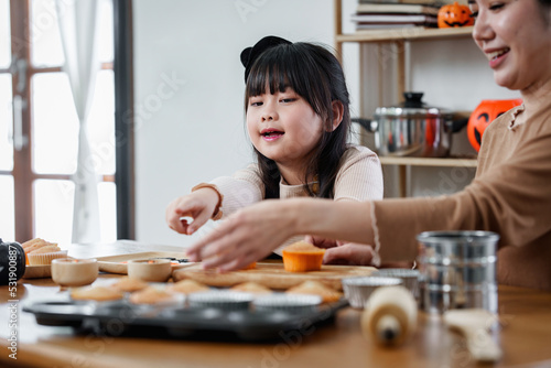 Young girl and mother at Halloween making treats and cupcake on table. Happy Halloween day