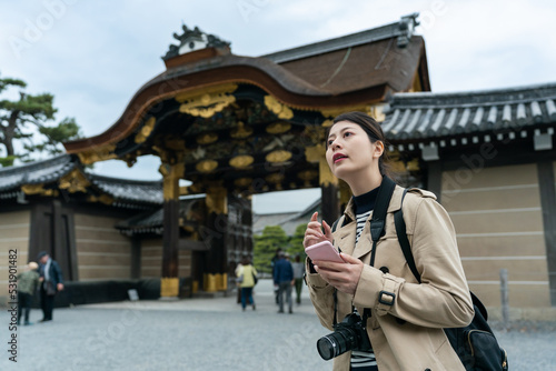 asian Korean woman tourist looking into distance while learning about travel information of Karamon Gate with phone app at nijo castle in Kyoto japan photo