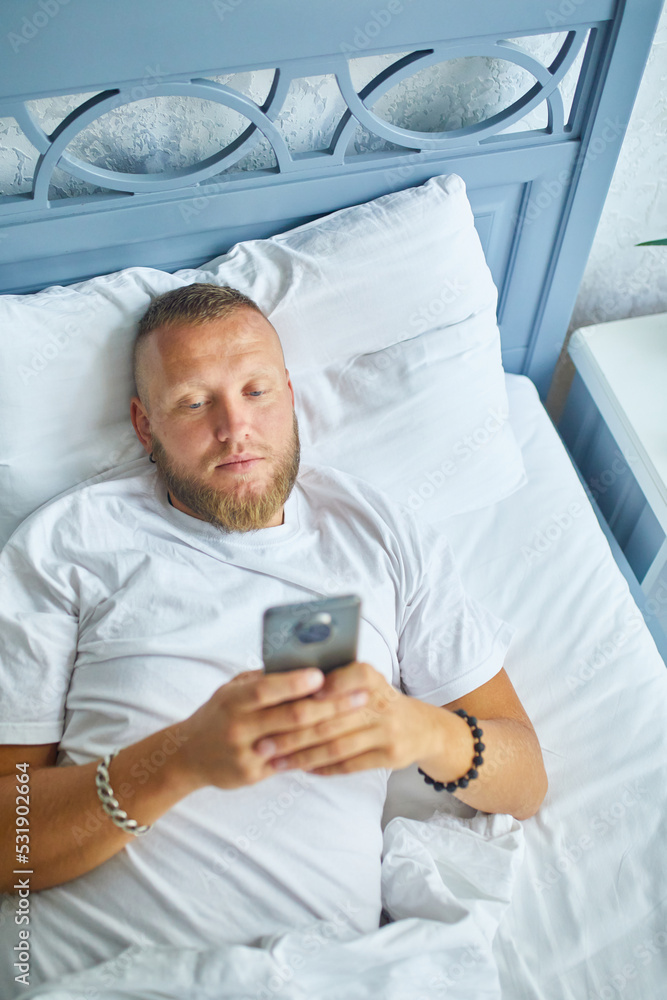 Bearded man using smartphone in morning in cozy while lying on bed Bearded man using smartphone in morning in cozy while lying on bed