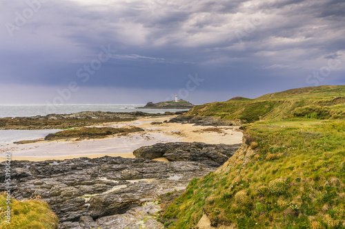 Clifftop view of the rock formations on Godrevy beach in Cornwall. In the distance under stormy skies is the Island with Godrevy Lighthouse