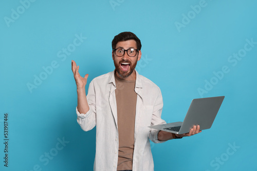 Emotional man with laptop on light blue background