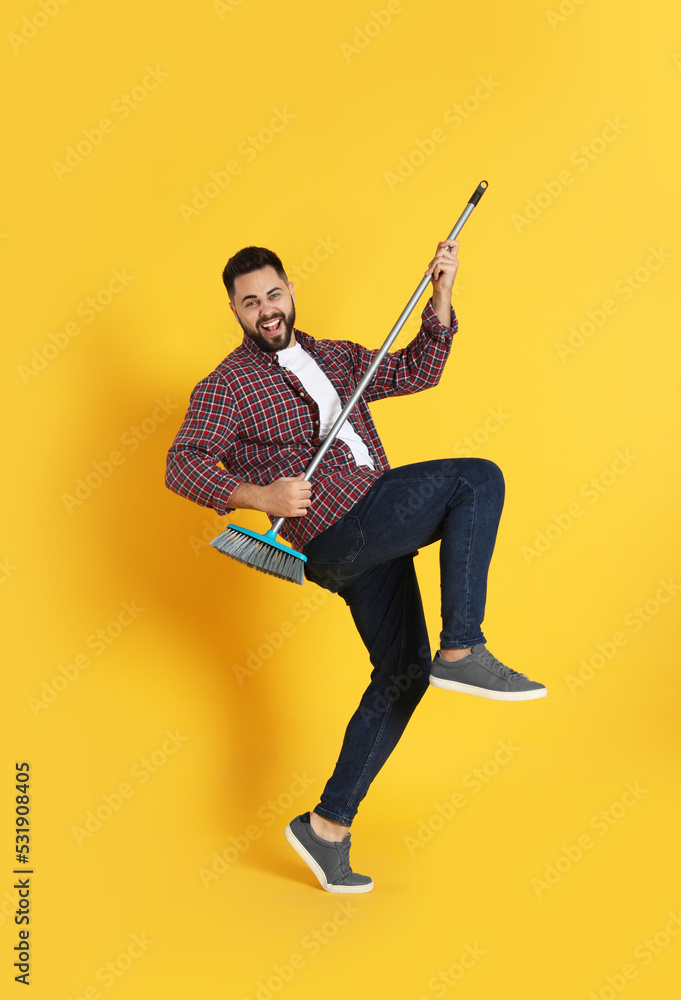 Young man with broom having fun on orange background Young man with broom having fun on orange background