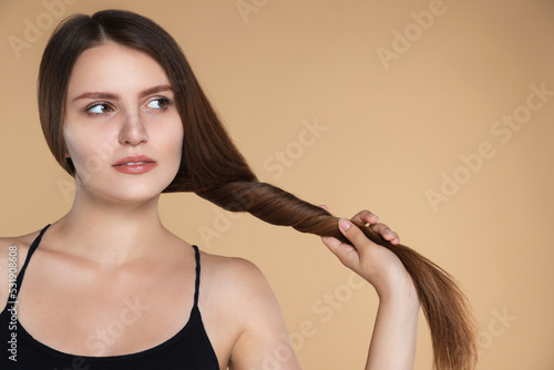 Young woman with strong healthy hair on beige background, space for text