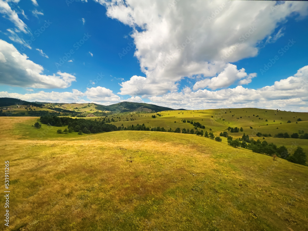 Obraz premium Beautiful white clouds are flowing across the sky over the green Zlatibor hills landscape on sunny summer day