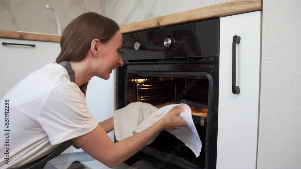 Woman taking tray of fresh cookies out of oven at home in the kitchen. Woman taking tray of fresh cookies out of oven at home in the kitchen.