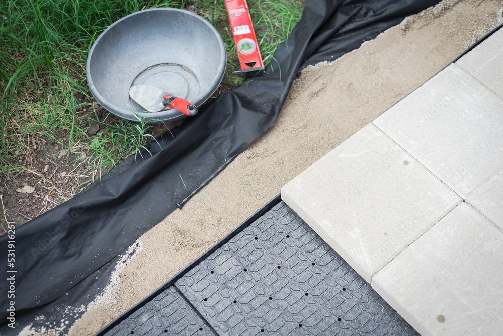 DIY sidewalk project with trowel, level, weed barrier and leveling