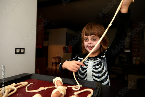 Cheerful kid in skeleton costume and makeup preparing pastries for baking on a baking sheet for the holiday halloween at home photo