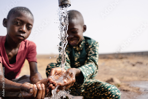 Canvas-taulu Two African toddlers playing with the water that flows from a rural faucet on th