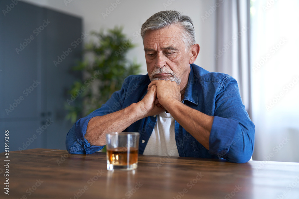 Senior caucasian man sitting and looking at the glass with whiskey at home Senior caucasian man sitting and looking at the glass with whiskey at home