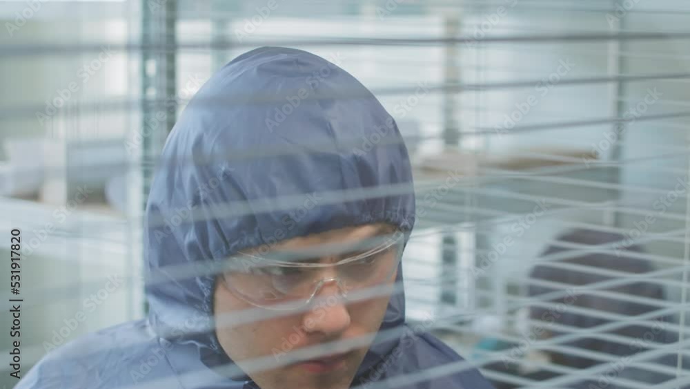 Young Asian male scientist engineer in protective blue coveralls and safety glasses working on research in laboratory Young Asian male scientist engineer in protective blue coveralls and safety glasses working on research in laboratory