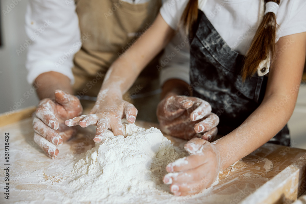 Fototapeta premium Close-up shot kid's hands and man's playing with flour on wooden surface. Sieving kneading process.