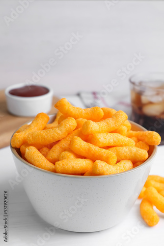 Crunchy cheesy corn snack in bowl on white wooden table, closeup