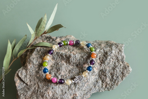 Bracelet made of natural multicolor stones beads on green background. Handmade jewelry. Woman exoteric accessories. Talismans and amulets. Selective focus © Lyubov