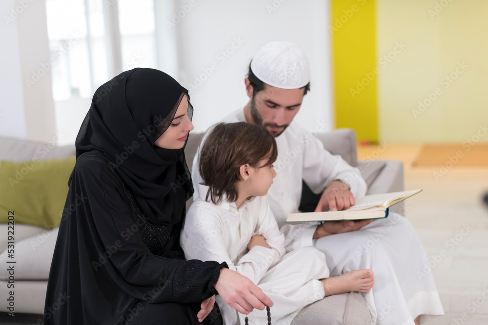 Traditional muslim family parents with children reading Quran and praying together on the sofa before iftar dinner during a ramadan feast at home Traditional muslim family parents with children reading Quran and praying together on the sofa before iftar dinner during a ramadan feast at home