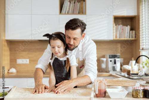 Curious daughter child kid cooking with father kneading rolling dough with hands for baking cooking homemade pizza in modern kitchen at home.