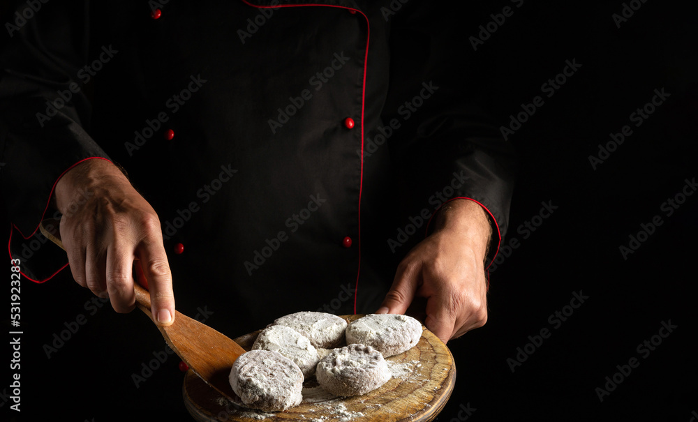 Meat cutlets with veal in flour on a cutting board in the hands of a chef. Free space for advertising on a black background