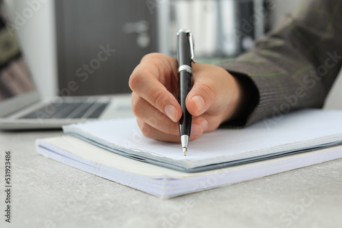 Woman writing in notebook at table indoors, closeup