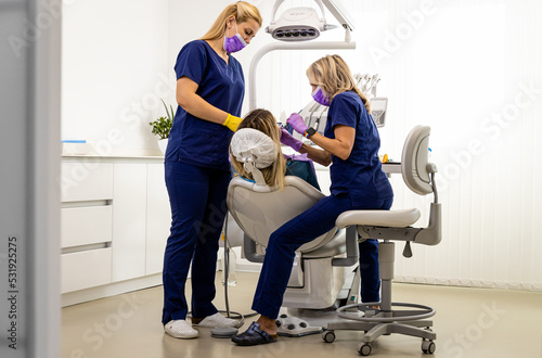 Female dentist with assistant working in dental clinic examining patient teeth.