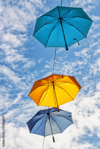 Colorful umbrellas in the air against blue sky with clouds © e_polischuk