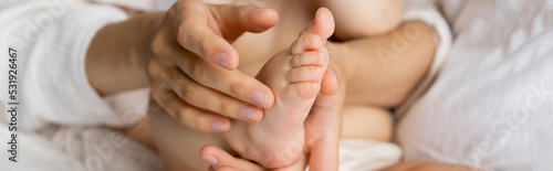 Cropped view of woman touching foot of infant daughter on blurred bed, banner.
