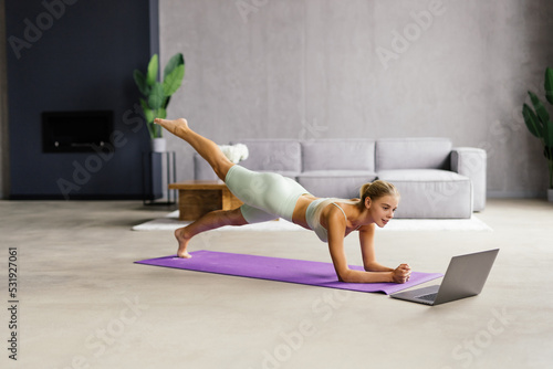 Tablou canvas Fit young woman doing yoga plank and watching online tutorials on laptop, traini