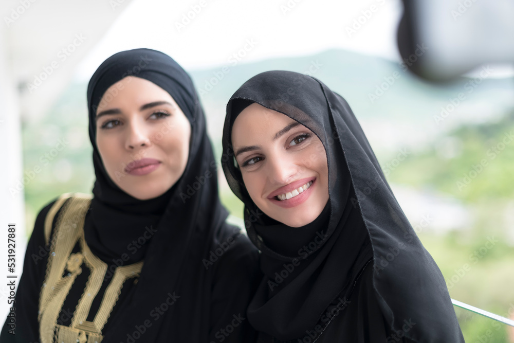 young beautiful muslim women in fashionable dress with hijab using mobile phone while taking selfie picture on the balcony representing modern islam fashion technology and ramadan kareem concept young beautiful muslim women in fashionable dress with hijab using mobile phone while taking selfie picture on the balcony representing modern islam fashion technology and ramadan kareem concept