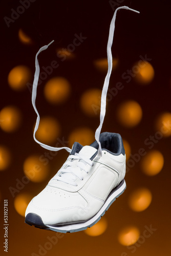 Fashion and Lifestyle Concepts. One New White Sneaker With Flying Shoelaces Placed Over Yellow Background With Circular Spotlights.