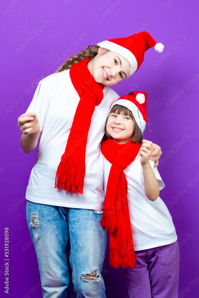 Two Embracing Positive Exclaiming Caucasian Girlfriends in Seasonal Warm Clothing Having Fun With Vivid Bright Burning Bengal Lights On Purple Background. Two Embracing Positive Exclaiming Caucasian Girlfriends in Seasonal Warm Clothing Having Fun With Vivid Bright Burning Bengal Lights On Purple Background.