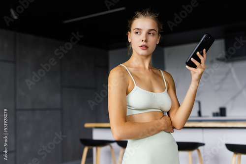 Beautiful fit woman looking at smartphone, listening music and relaxing after training