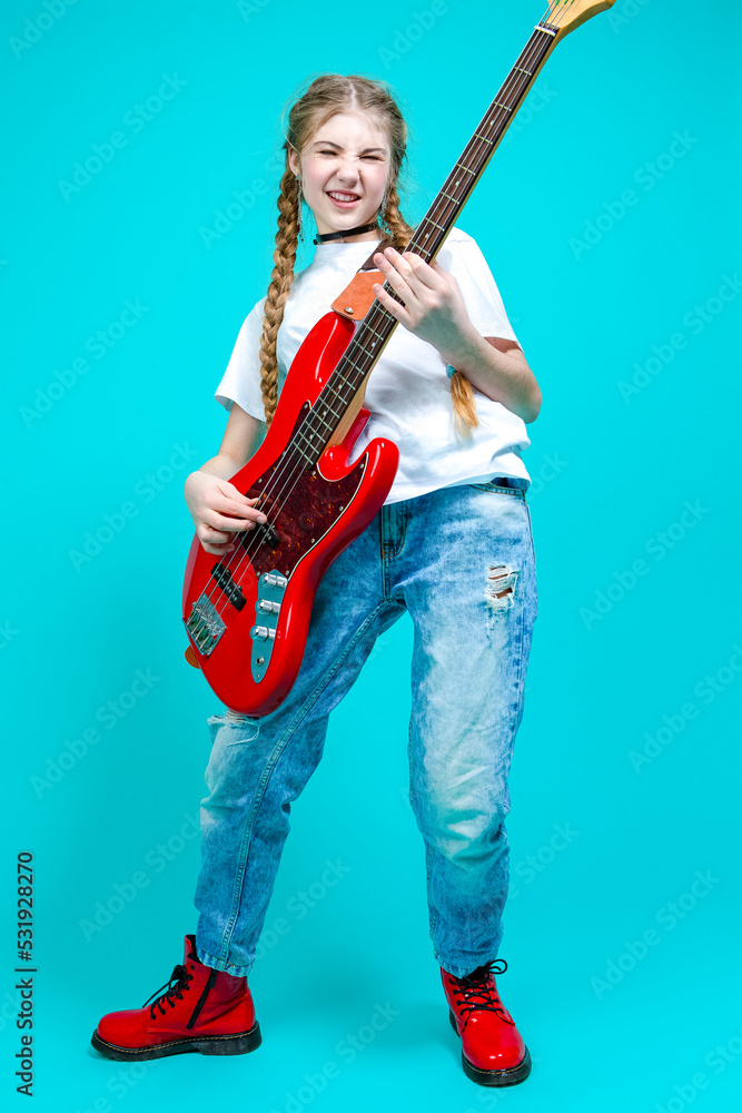 Caucasian Teenager Guitar Player With Red Shiny Bass Guitar Posing In Casual White Shirt Showing Pleased Expression On Turquoise Background. Caucasian Teenager Guitar Player With Red Shiny Bass Guitar Posing In Casual White Shirt Showing Pleased Expression On Turquoise Background.