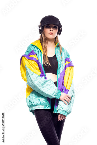 Winsome Sportwoman in Fitness Outfit and Baseball Cap With Wireless Headphones Listening Music While Looking Straight With Hands Crossed In Front Over White. photo