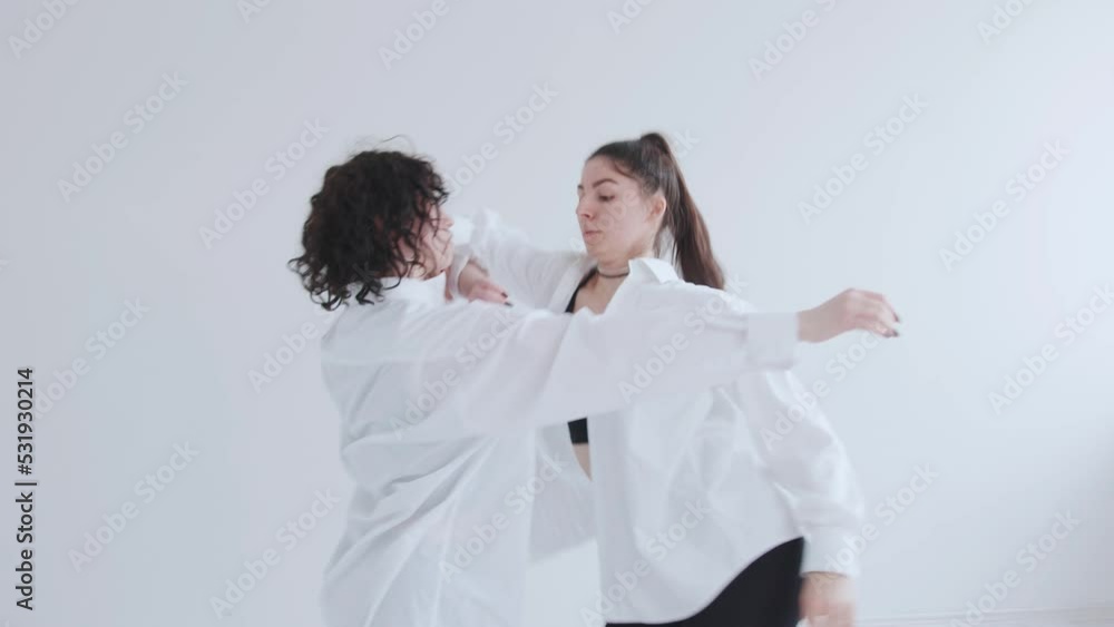 Two beautiful young girls perform an avant-garde modern dance in a white studio and contact each other in motion Two beautiful young girls perform an avant-garde modern dance in a white studio and contact each other in motion