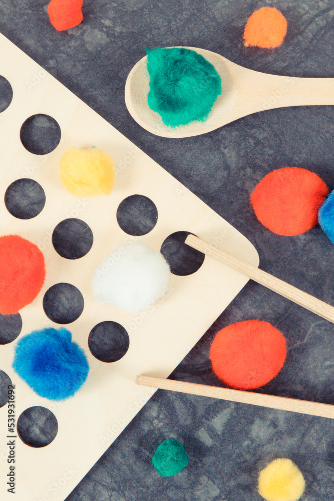 Colorful pompoms with spoon and tongs. Development of kids motor skills, coordination, creativity and logical thinking Colorful pompoms with spoon and tongs. Development of kids motor skills, coordination, creativity and logical thinking