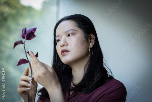 Curious young woman holding plant with burgundy leaves