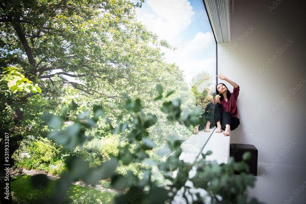Young woman sitting in window with view of green trees Young woman sitting in window with view of green trees