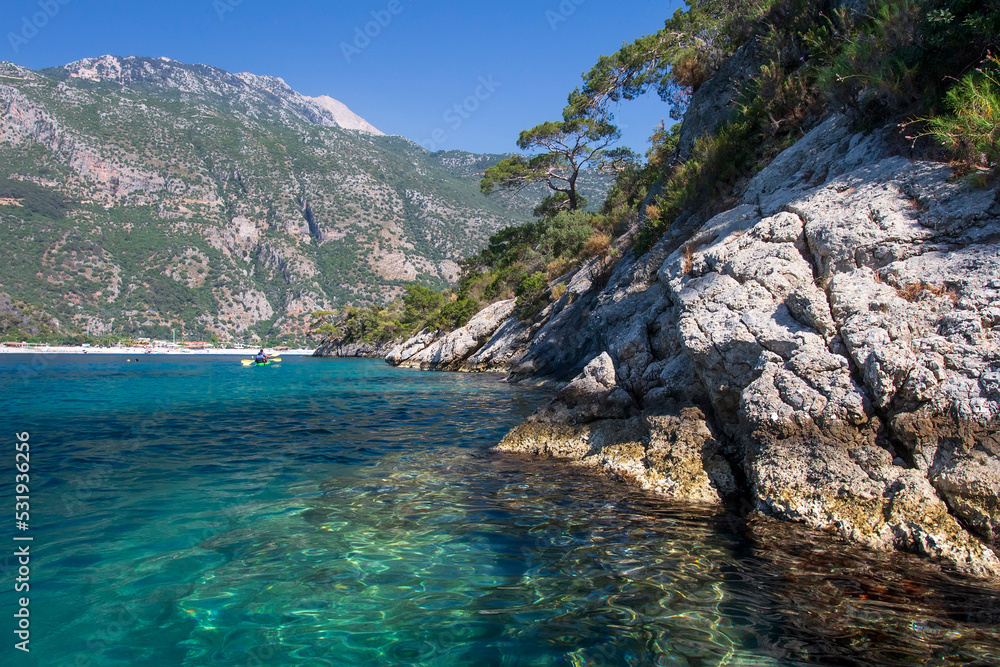 Beautiful landscape on the sea, the rocky coast, view on the mountains and small boat with people. Blue lagoon in Oludeniz, Turkey. Small boats on clear water. Tourism.