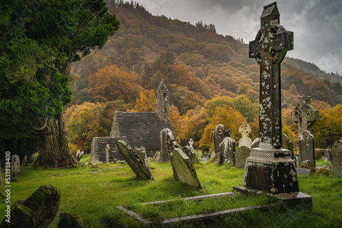 Medieval church ancient graves Celtic crosses in Glendalough Cemetery. Moody autumn forest, mountains in rain, storm sky in background Wicklow Ireland