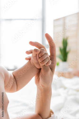 Cropped view of child holding finger of mother in blurred bedroom.