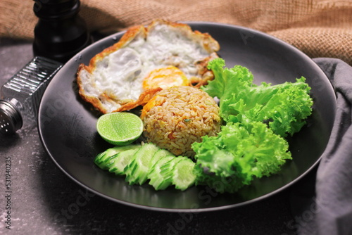 Fried rice in black plate with fried egg, lettuce and cucumber.