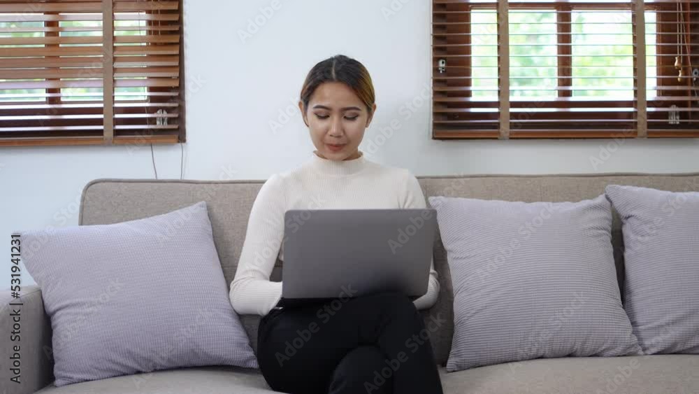 Beautiful Asian businesswoman sitting comfortably on sofa at home with laptop and bright smile of a new day. Beautiful Asian businesswoman sitting comfortably on sofa at home with laptop and bright smile of a new day.