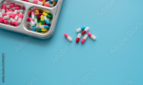 High-angle view of multi-colored antibiotic capsule pills on stainless steel tray and blue background. Antibiotic drug resistance. Prescription drugs. Pharmaceutical industry. Healthcare and medicine.