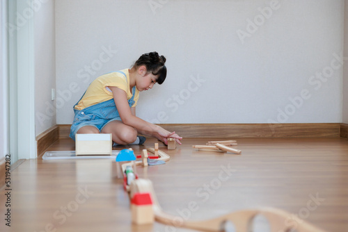 Asian cute girl playing wood block building rail way and road on the floor at home.