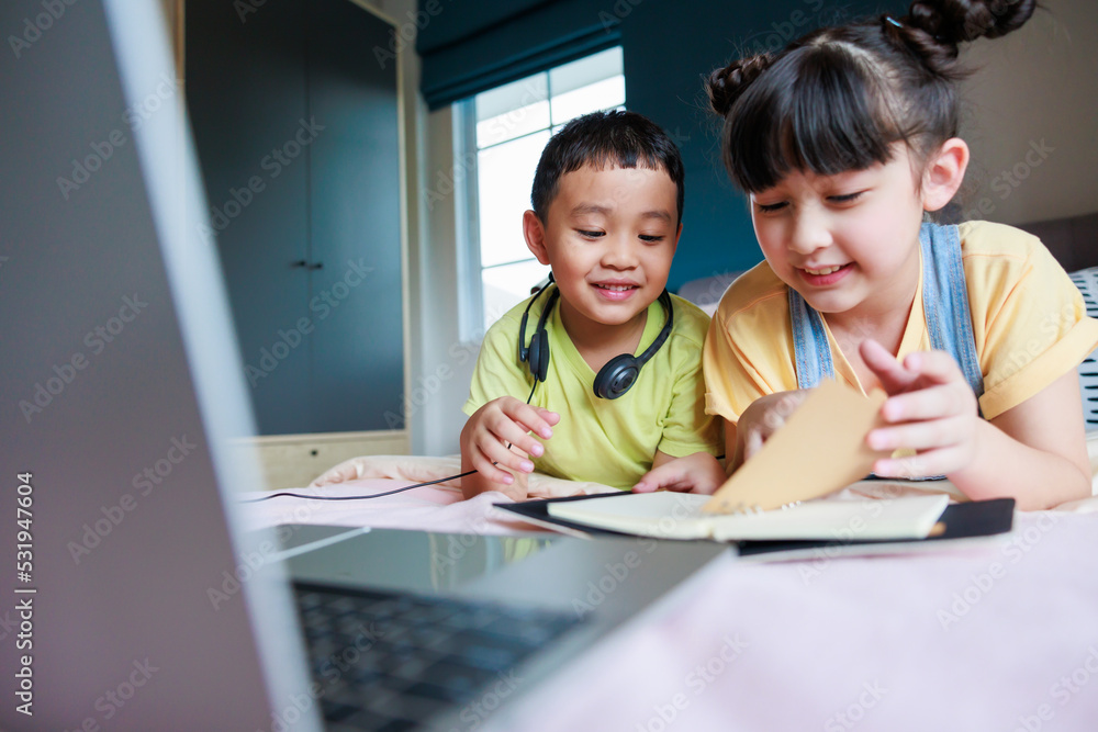 Cute asian older sister teach brother reading book and telling funny stories. Brother using headphone and laptop for find interesting thing. Cute asian older sister teach brother reading book and telling funny stories. Brother using headphone and laptop for find interesting thing.