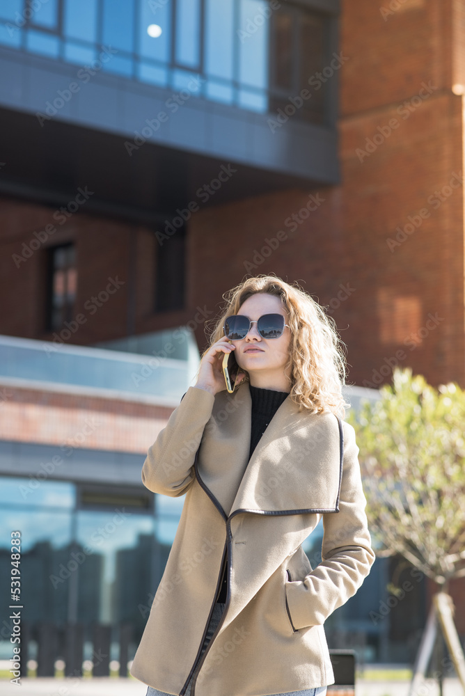 A young blonde girl is talking on her mobile phone about work while walking in the city in autumn.