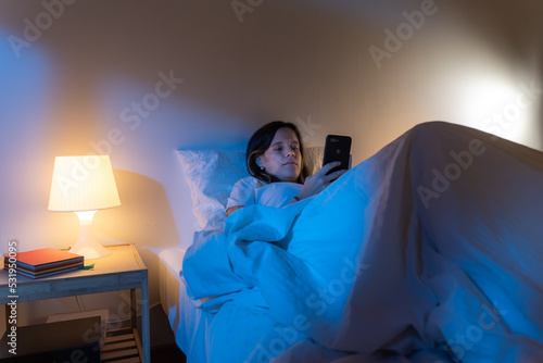 Girl looking her smart phone doom scrolling on bed in the middle of the night. Technology at bed concept.