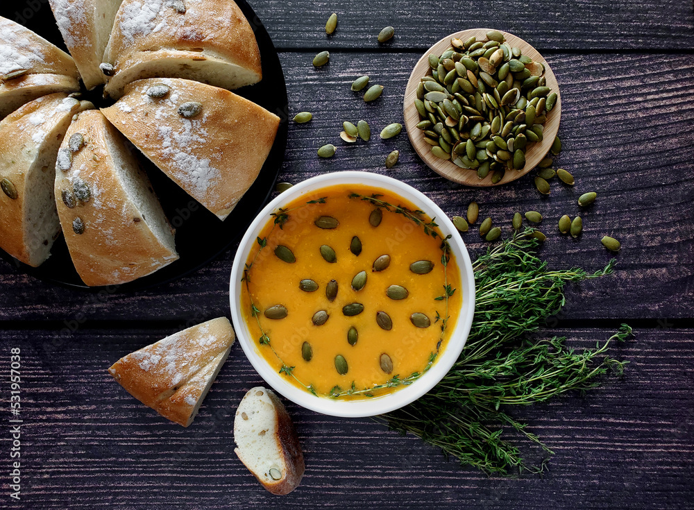 Pumpkin cream soup with pumpkin seeds and thyme, pumpkin bread. Wooden background, top view. Pumpkin cream soup with pumpkin seeds and thyme, pumpkin bread. Wooden background, top view.